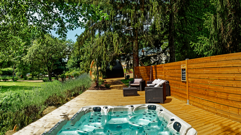 Jacuzzi umgeben von warmer Holzterrasse und Wiese mit Bäumen 