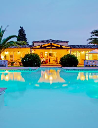 Beleuchteter Pool am Abend vor einem mediterranen Gebäude mit Palmen