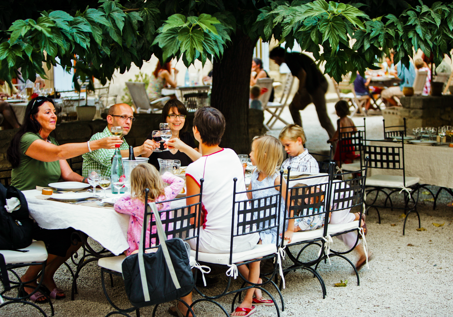 Familie sitzt unter Bäumen an einem Tisch im Freien beim Essen