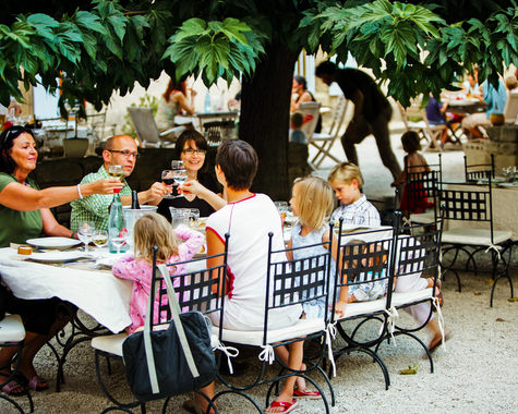 Familie sitzt unter Bäumen an einem Tisch im Freien beim Essen