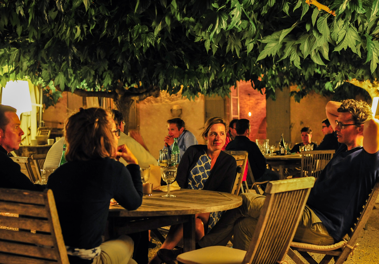 Gruppe von Menschen sitzt abends gemeinsam an einem Tisch im Garten