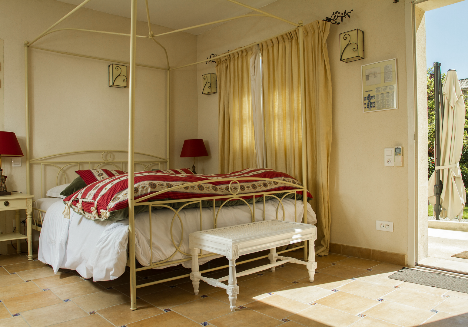Weißes Metallbett mit roter Decke und Blick in den Garten