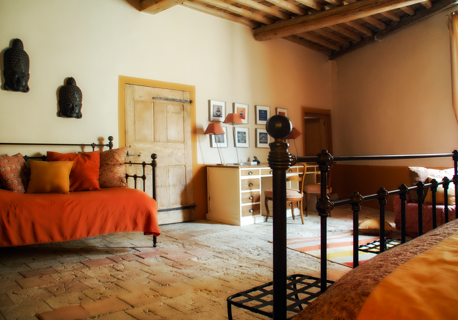 Schlafzimmer mit orangefarbener Bettwäsche, Holzbett und Terrakottaboden