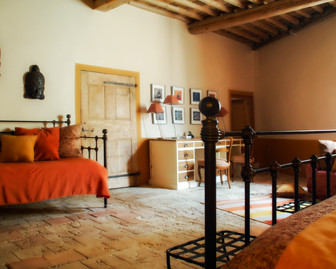 Schlafzimmer mit orangefarbener Bettwäsche, Holzbett und Terrakottaboden