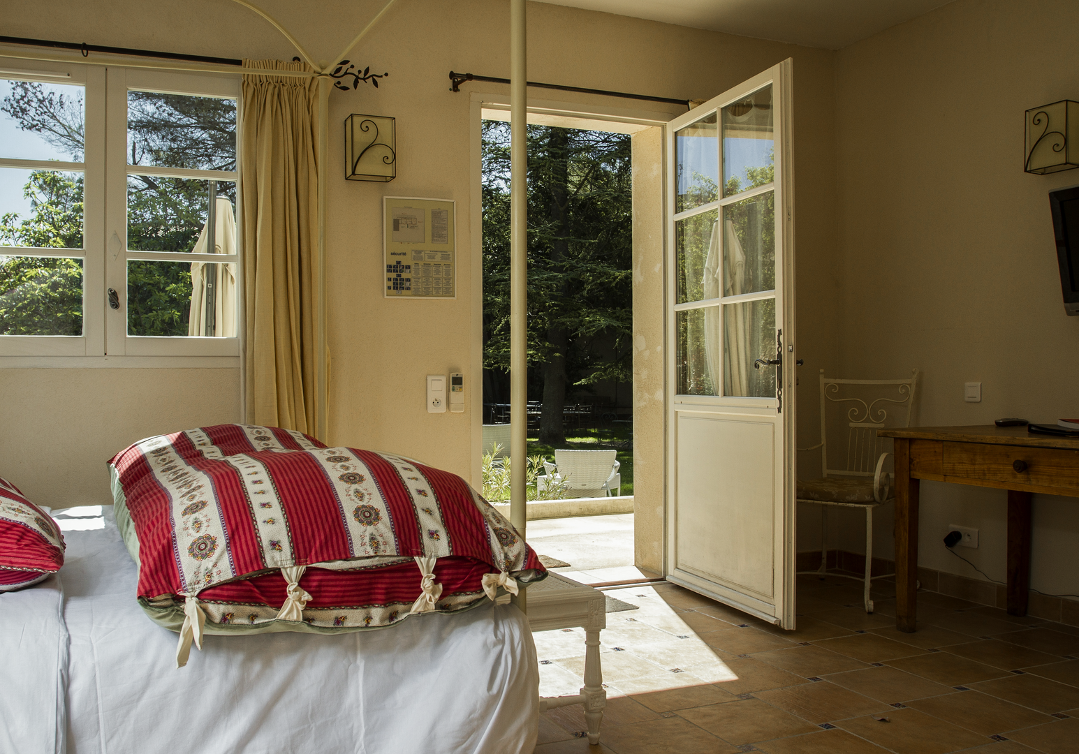 Schlafzimmer mit roter Bettwäsche, offener Tür und Gartenblick
