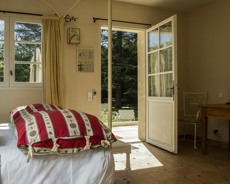 Schlafzimmer mit roter Bettwäsche, offener Tür und Gartenblick