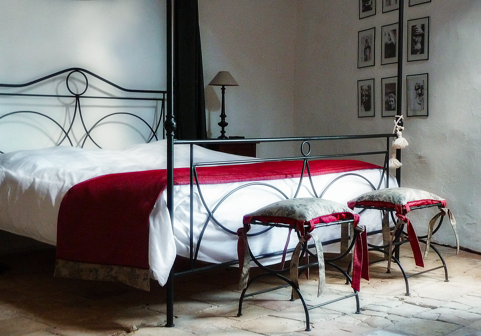 Metallbett mit roter Decke, Hocker und Bilderrahmen an der Wand