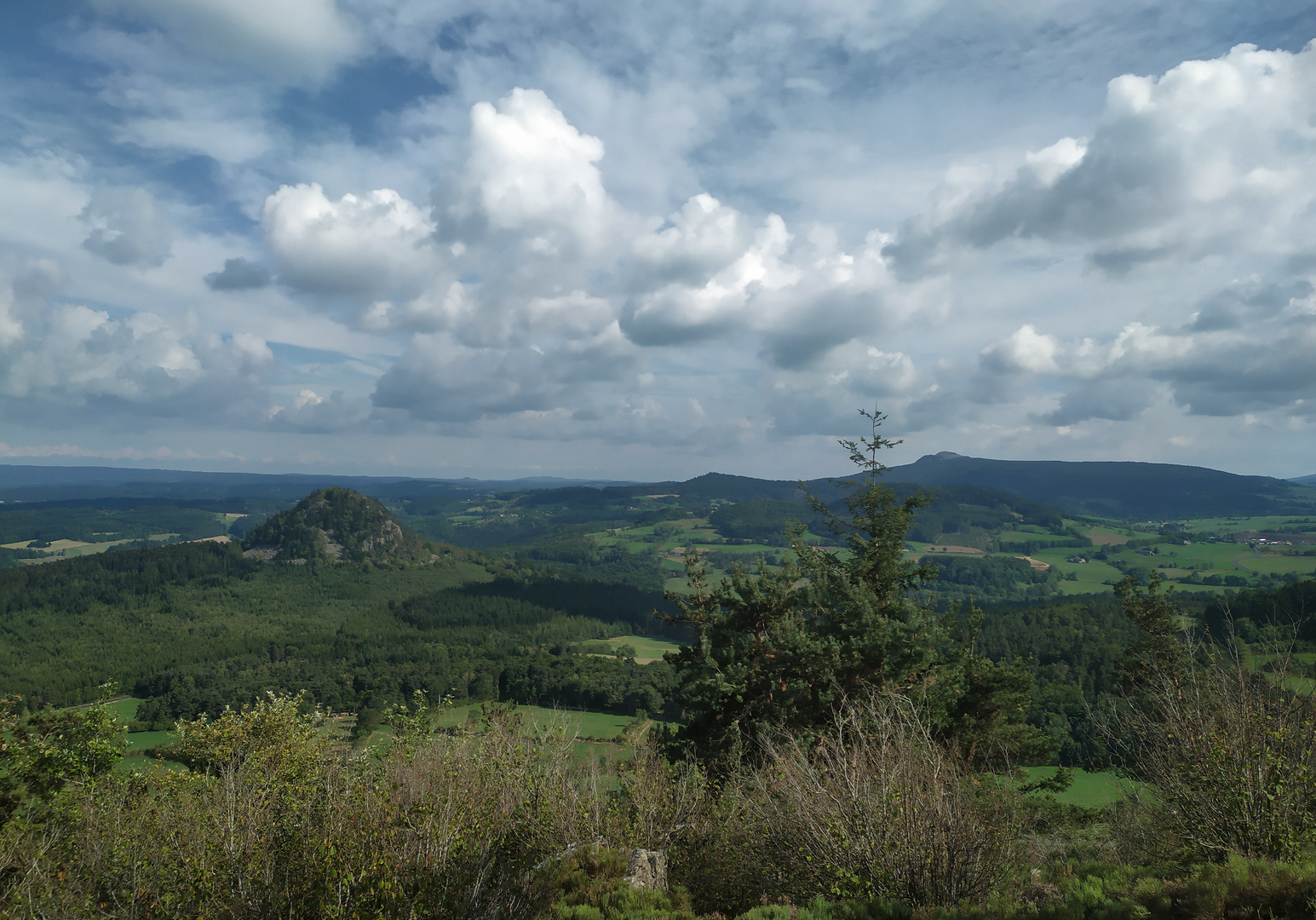 Weite Landschaft unter wolkigem Himmel mit Blick über grüne Hügel