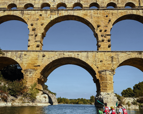 Historisches Aquädukt mit großen Bögen überspannt einen Fluss wo Personen paddeln