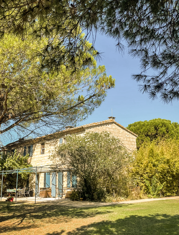 Haus mit Garten und Bäumen unter blauem Himmel in sonniger Landschaft