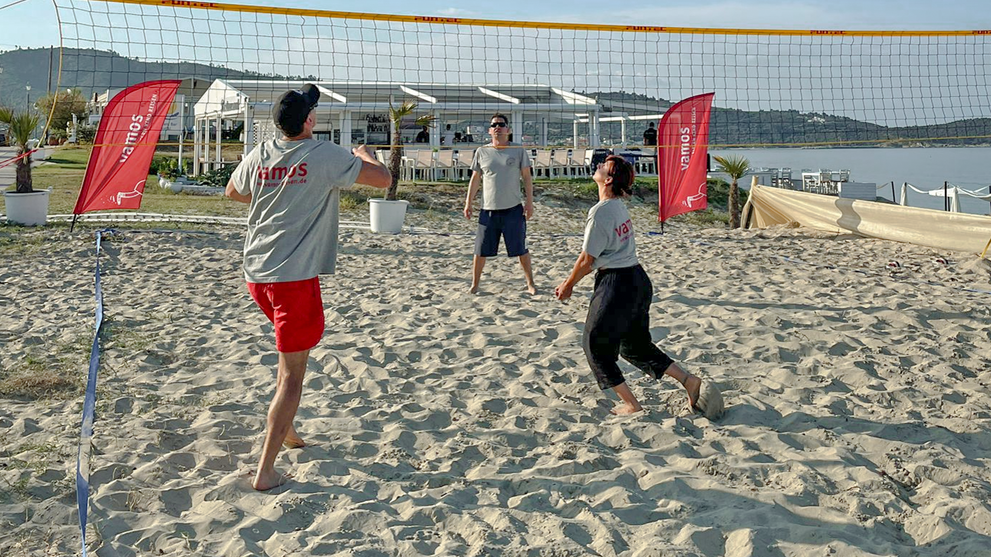 Personen spielen gemeinsam Volleyball am Sandstrand unter blauem Himmel