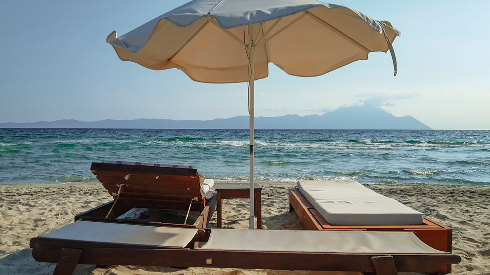 Sonnenliegen mit Sonnenschirm direkt am Sandstrand und Meerblick