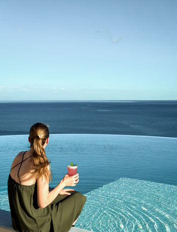 Frau sitzt am Infinity-Pool mit Blick auf das ruhige Meer