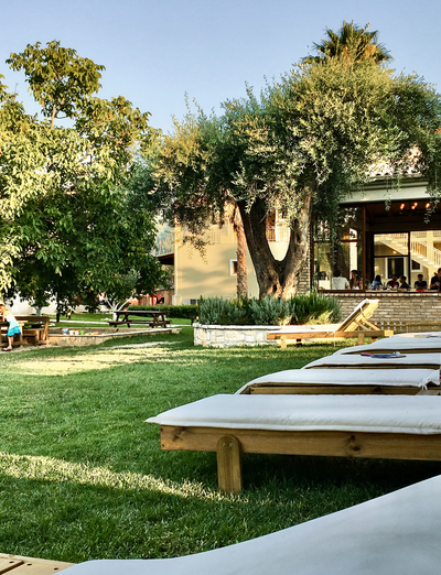 Liegestühle auf grüner Wiese vor mediterranem Landhaus im Schatten alter Bäume