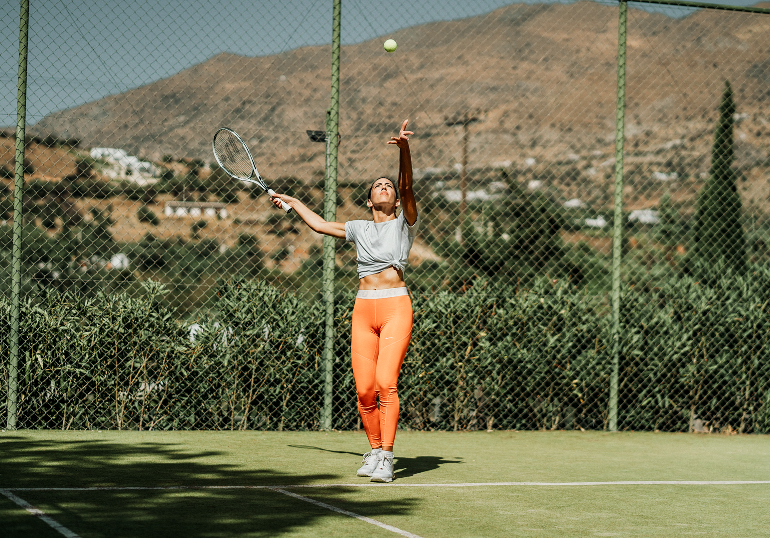 Frau steht auf Tennisplatz vor bergiger Landschaft