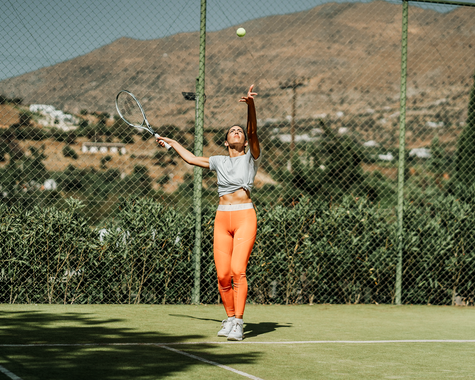 Frau steht auf Tennisplatz vor bergiger Landschaft