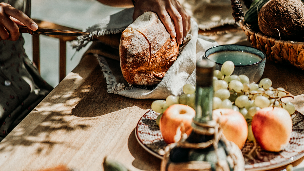 Frisches Brot wird auf einem sommerlich gedeckten Tisch geschnitten