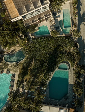 Luftaufnahme einer mediterranen Poollandschaft zwischen Palmen und Gebäuden