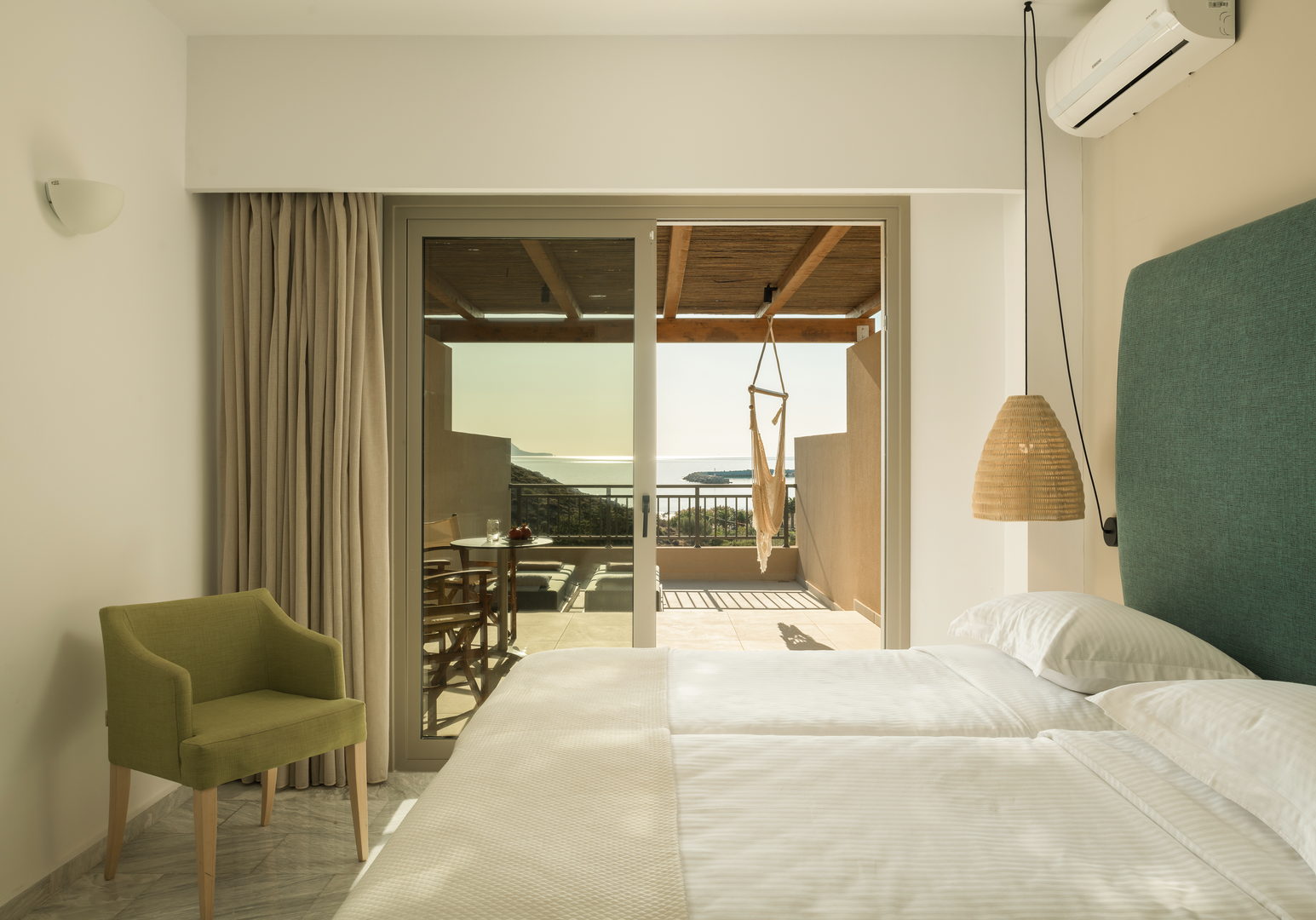 Schlafzimmer mit Doppelbett, grünem Sessel und Meerblick