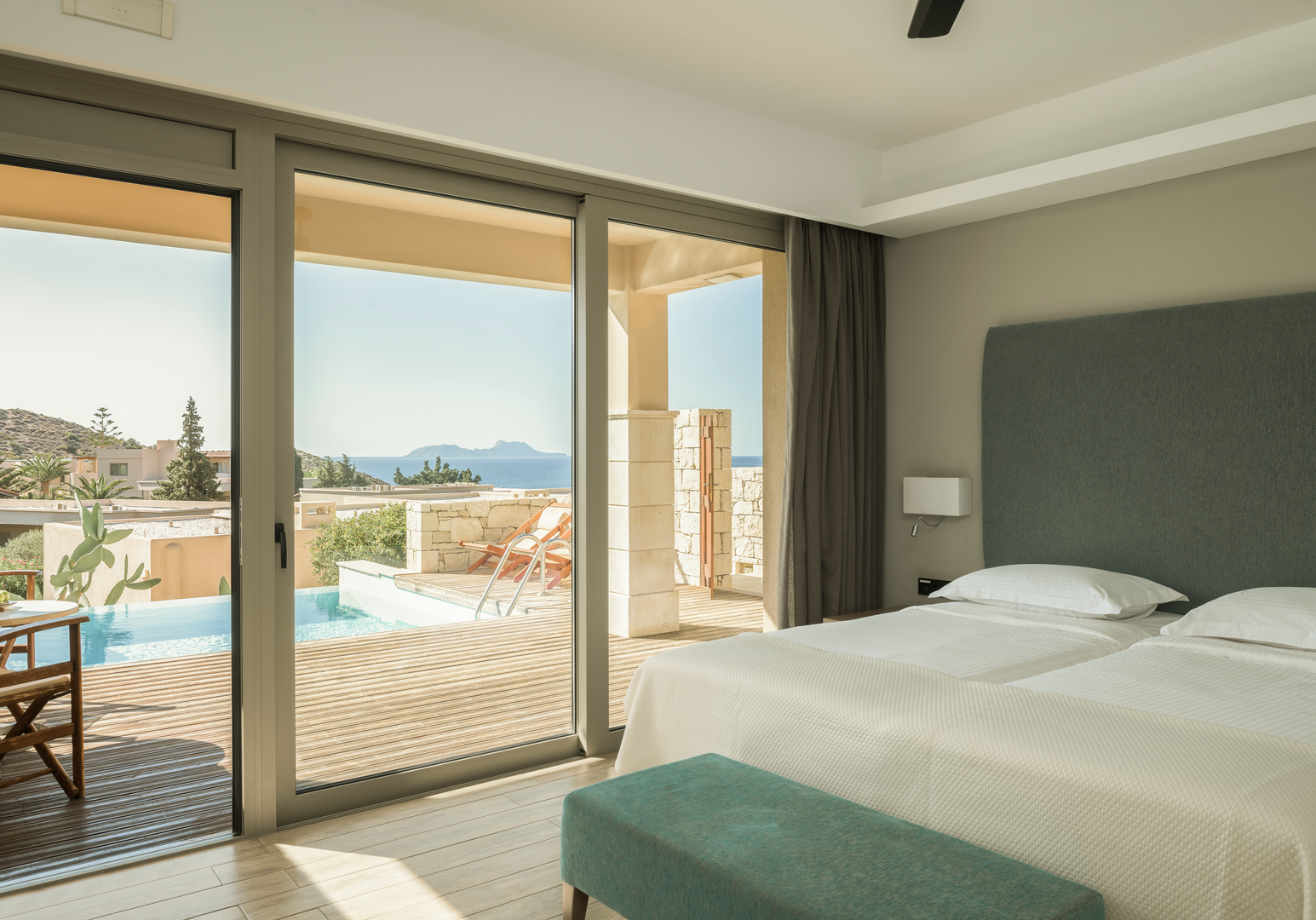 Doppelbett mit türkisem Kopfteil und Blick auf Pool und Meer