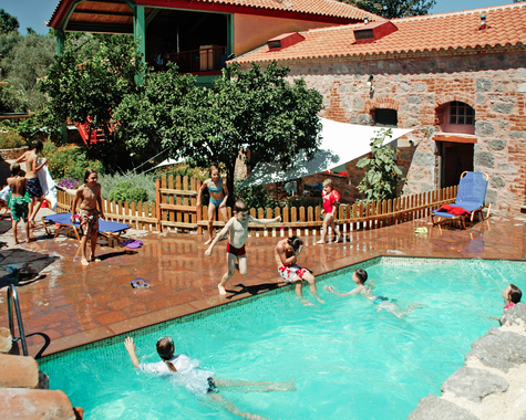 Poolbereich einer Ferienanlage mit Badegästen, Liegen und Gebäuden im Hintergrund.