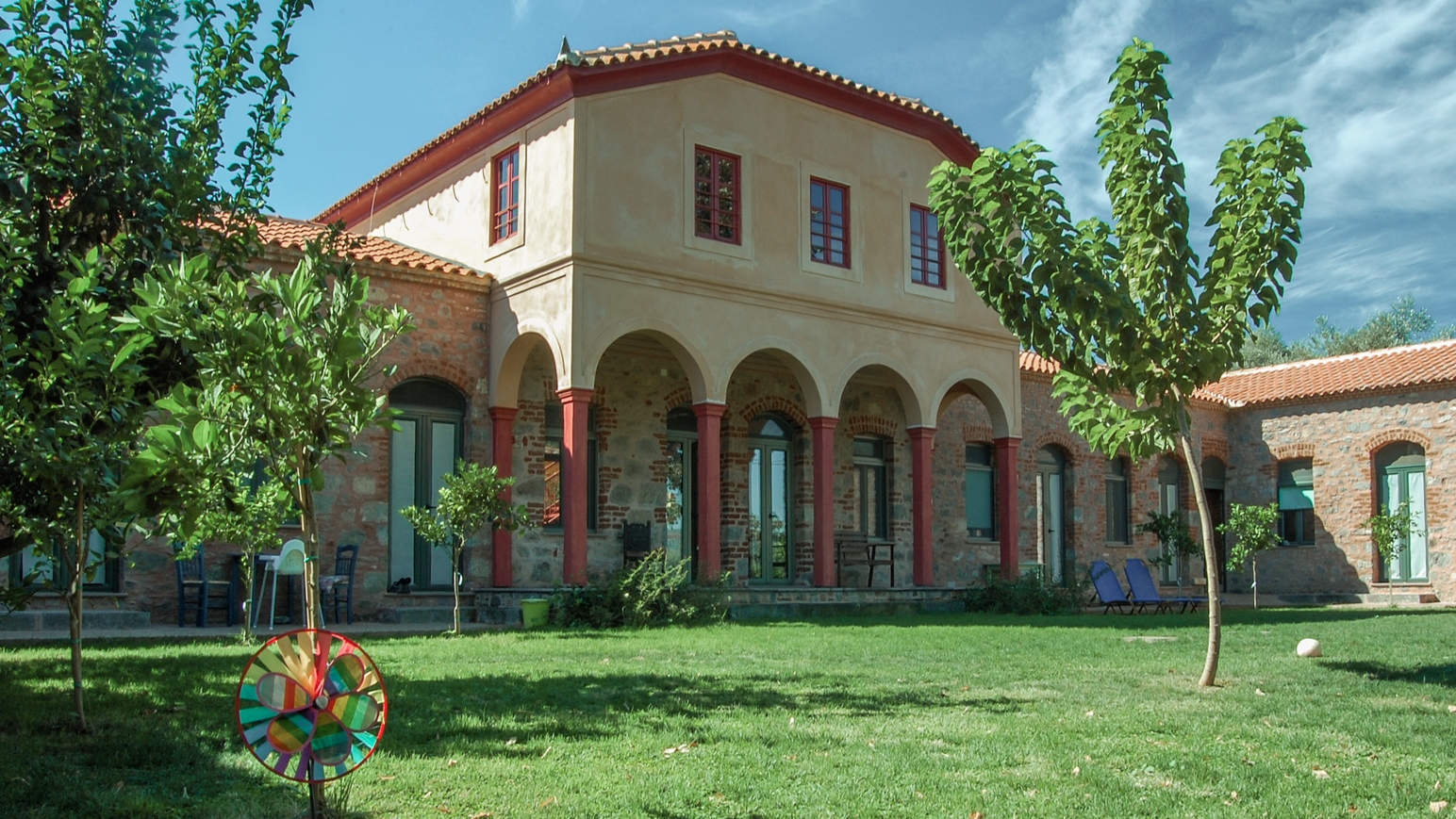 Große Gartenanlage mit Rasenfläche, Bäumen und mediterranem Gebäude.