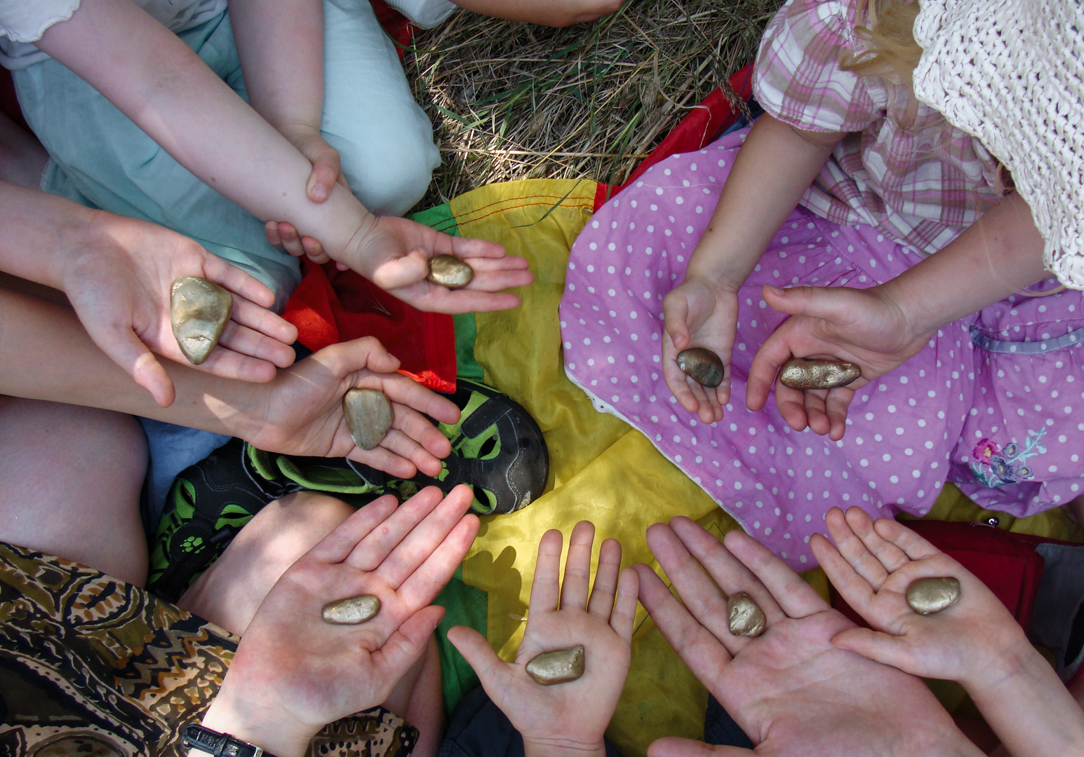 Kinderhände mit bemalten Steinen und Bastelmaterial auf bunten Tüchern.