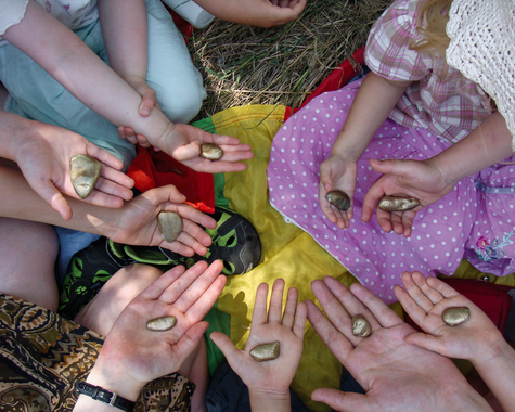 Kinderhände mit bemalten Steinen und Bastelmaterial auf bunten Tüchern.