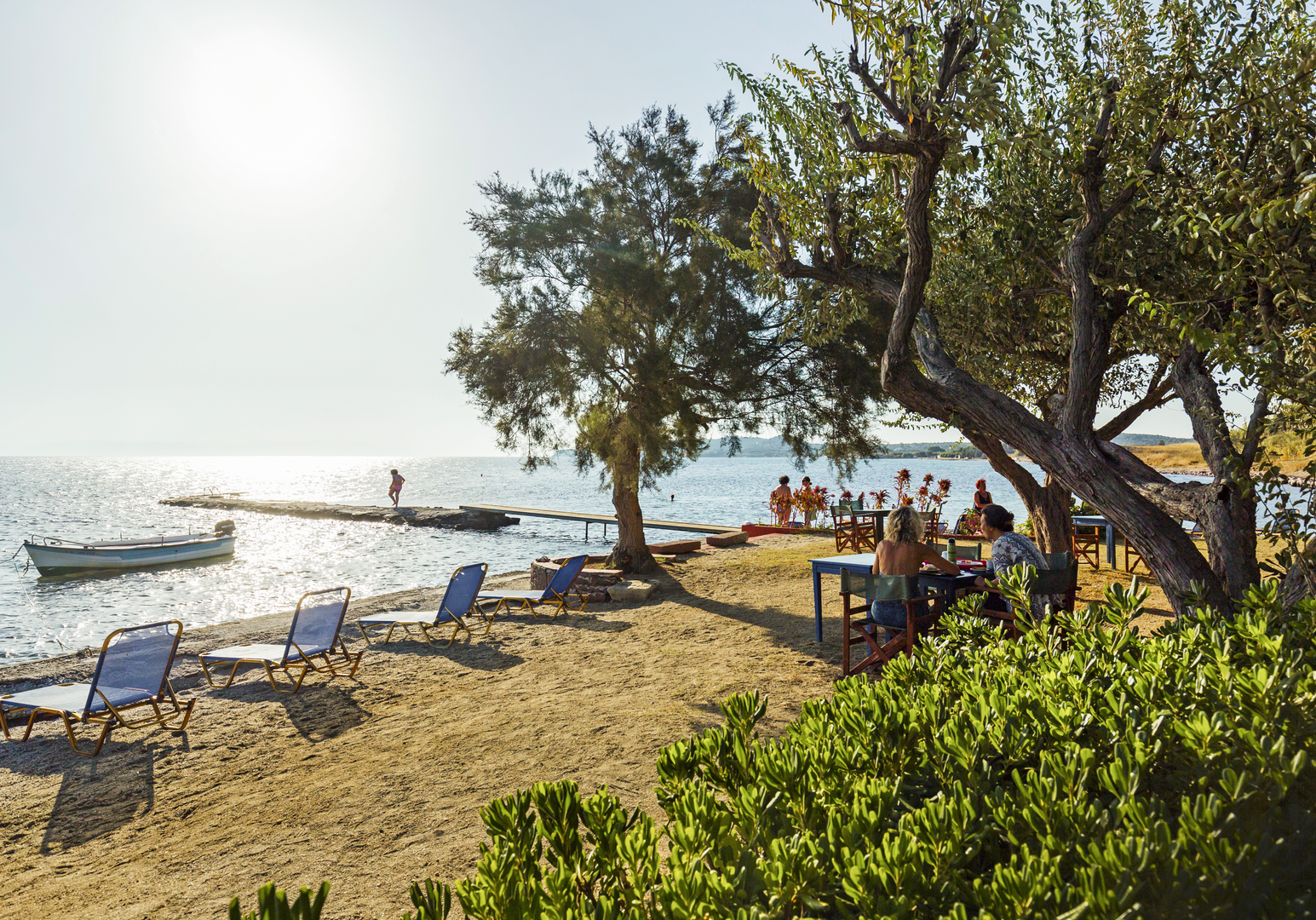 Küstenabschnitt mit Bäumen, Sonnenschirmen und Blick auf das Meer.