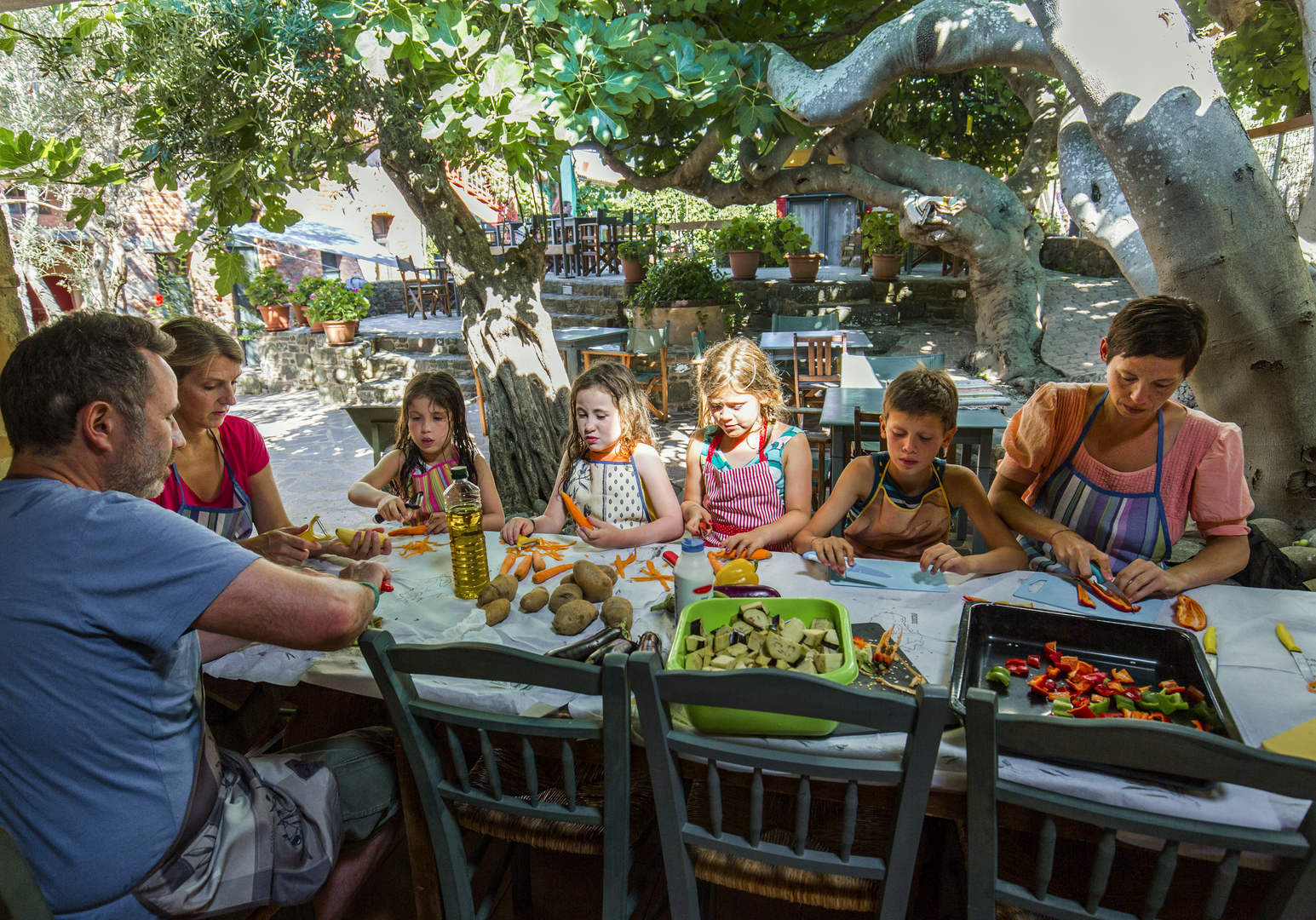 Gruppe von Kindern und Erwachsenen beim gemeinsamen Essen an einem langen Tisch im Freien.
