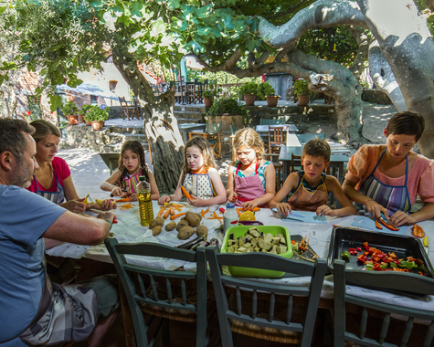 Gruppe von Kindern und Erwachsenen beim gemeinsamen Essen an einem langen Tisch im Freien.
