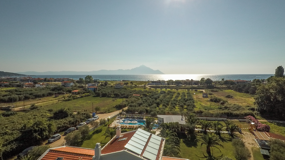 Luftaufnahme einer Ferienanlage mit Gebäuden, Pool und umliegender Landschaft nahe der Küste.