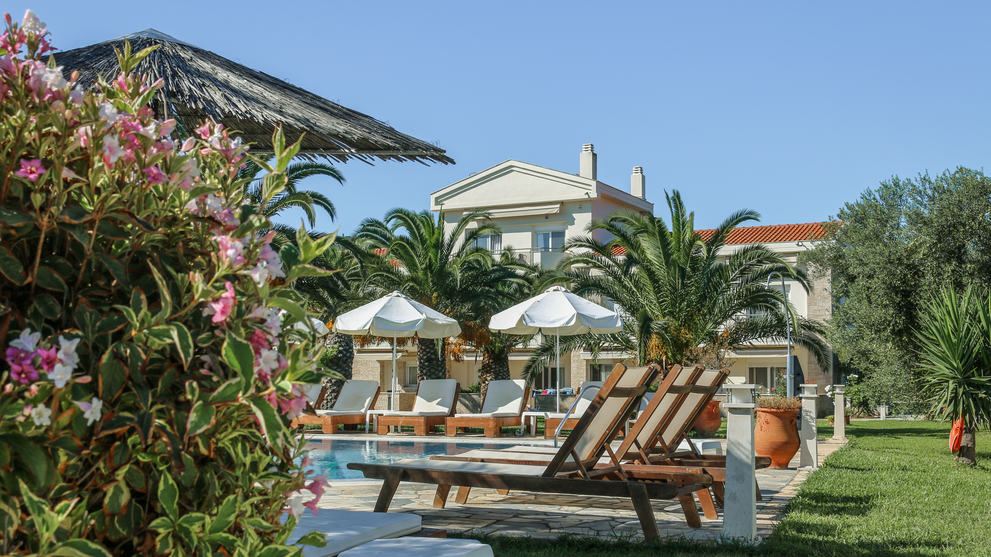 Poolbereich mit Liegen, Sonnenschirmen und Ferienanlage im Hintergrund.
