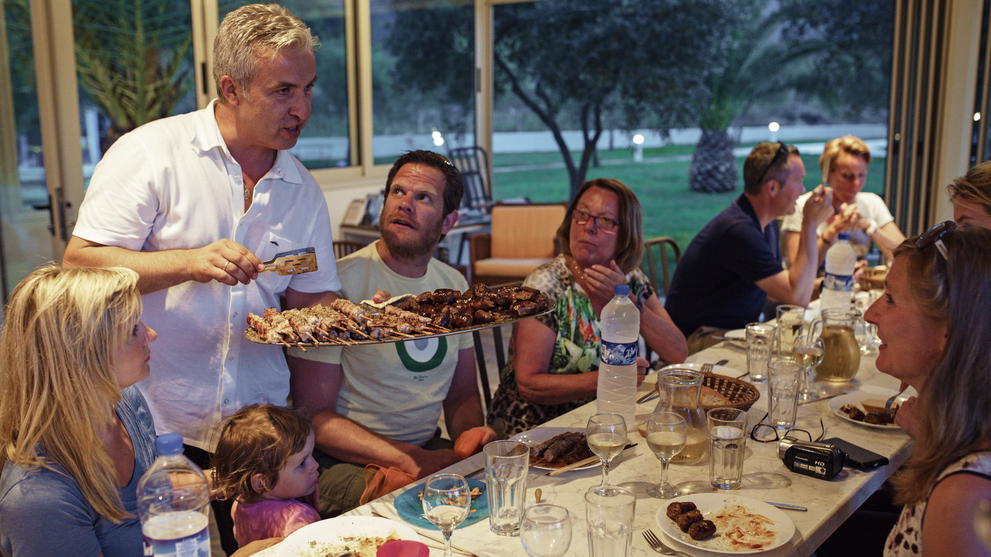 Familie sitzt gemeinsam an einem gedeckten Tisch beim Essen im Freien.