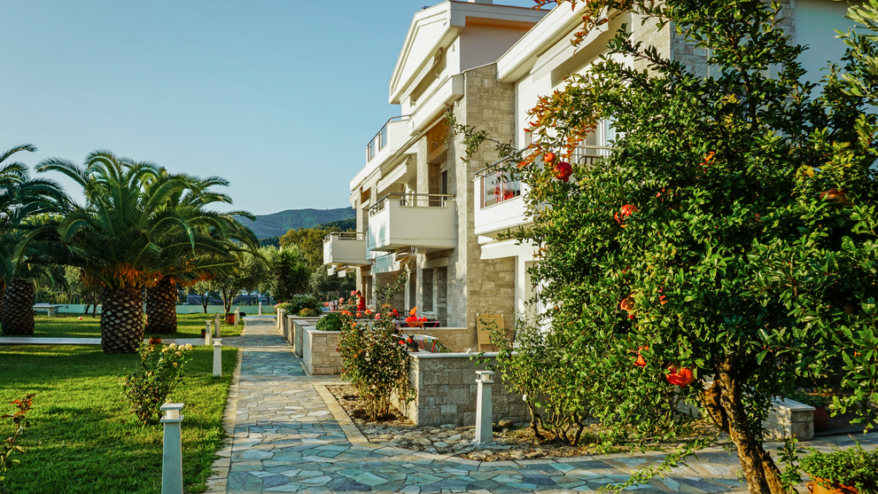 Ferienanlage mit mehrstöckigem Gebäude, Gartenweg und mediterraner Bepflanzung.