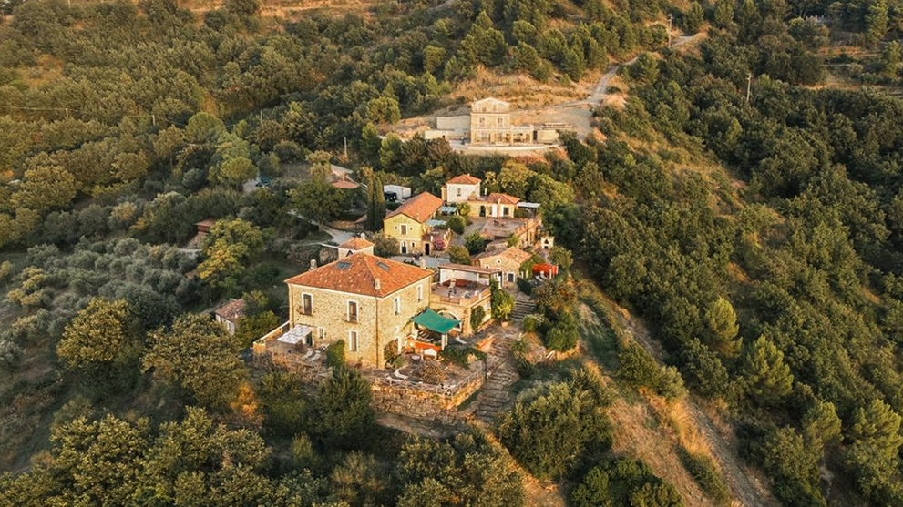 Luftaufnahme einer Ferienanlage auf einem bewaldeten Hügel in mediterraner Umgebung.