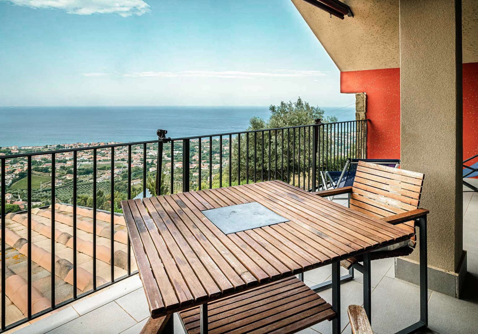 Balkon mit Holztisch, Stühlen und Blick auf die Küstenlandschaft und das Meer.