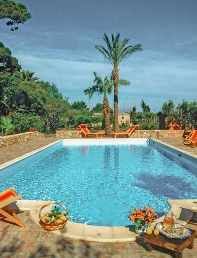 Poolbereich mit Liegen, Palmen und beleuchteter Gartenanlage.