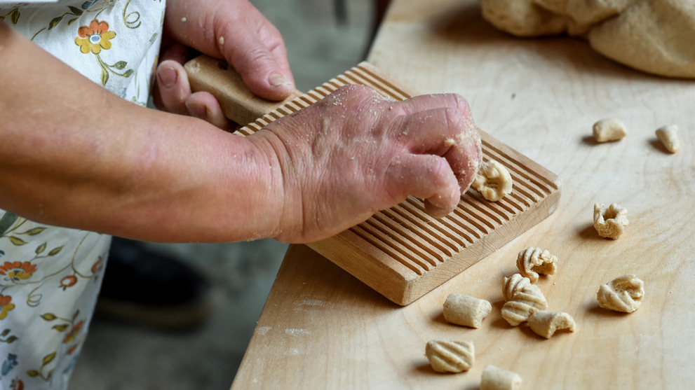 Hände bei der Zubereitung frischer Pasta auf einer traditionellen Holzarbeitsfläche.