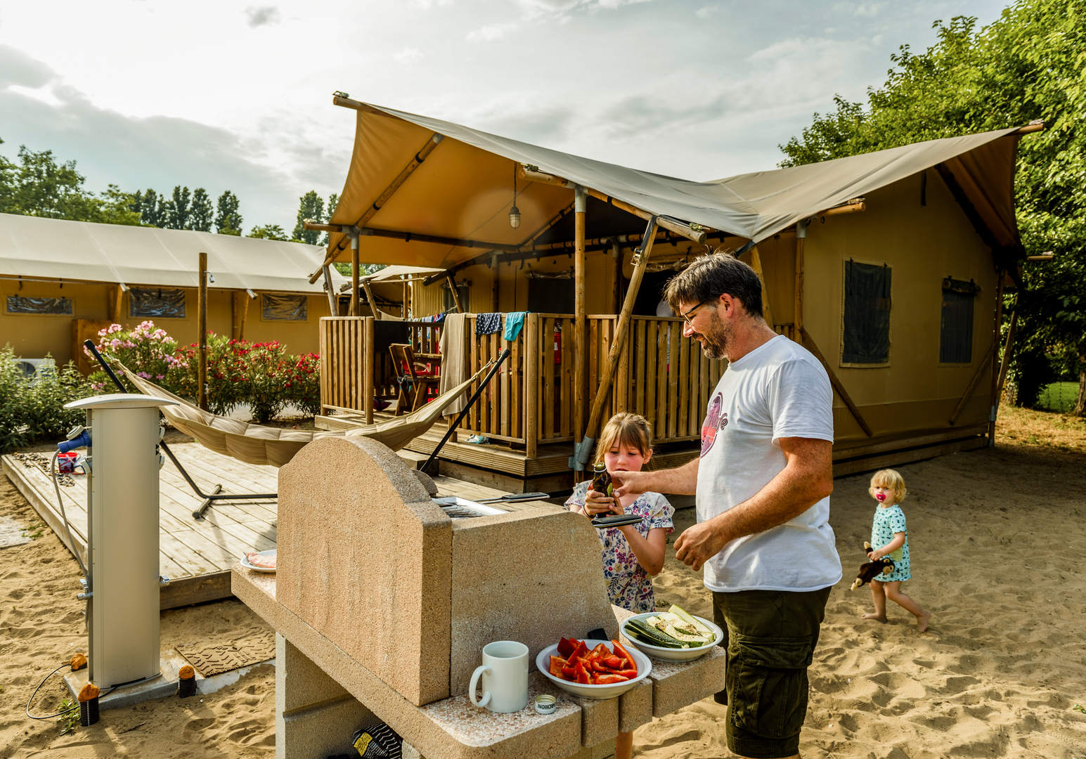Vater grillt gemeinsam mit Kindern vor einer Hütte 