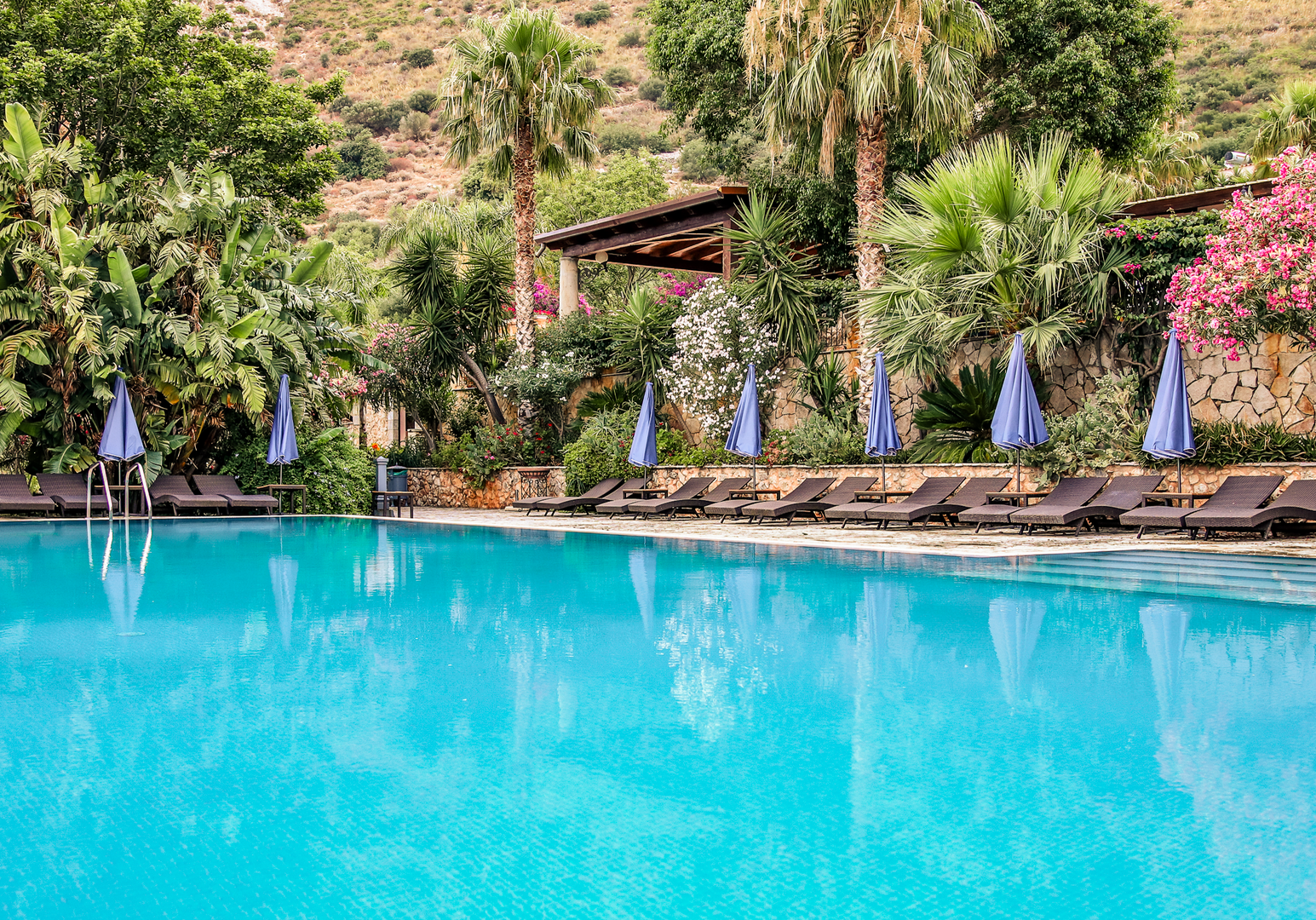 Swimmingpool mit Liegebereich in einer tropisch anmutenden Gartenanlage.