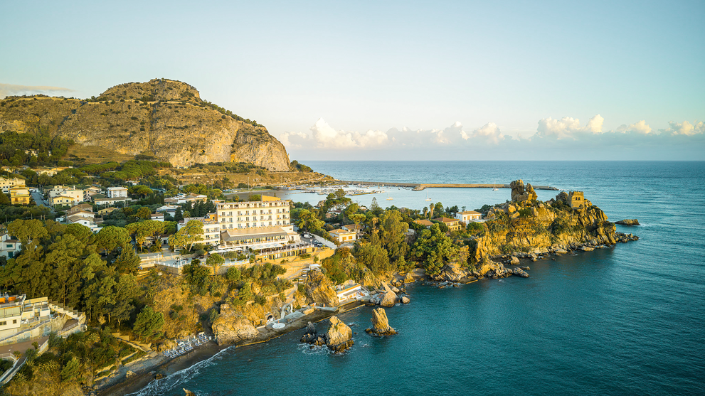 Panorama eines Küstenortes mit Hotels, Villen und einer geschützten Bucht vor dem Meer.