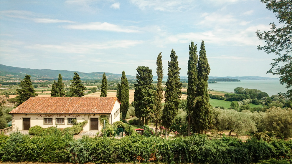 Landhaus mit Garten und Zypressen vor einer weiten Hügellandschaft.