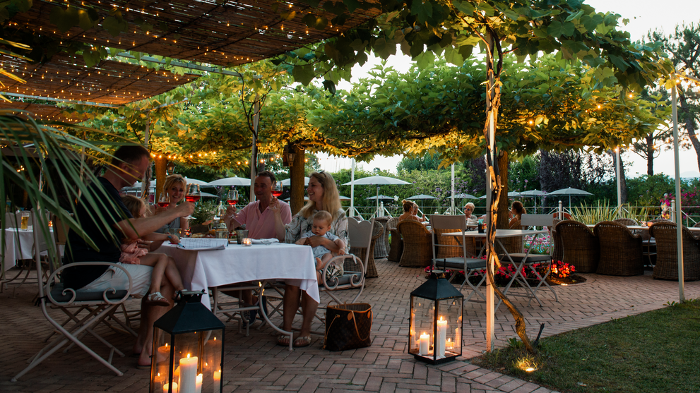 Gemütliche Restaurantterrasse mit stimmungsvoller Beleuchtung unter Bäumen in den Abendstunden.