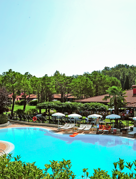 Poolanlage der Ferienanlage, eingebettet in eine weitläufige Gartenlandschaft mit Bäumen.