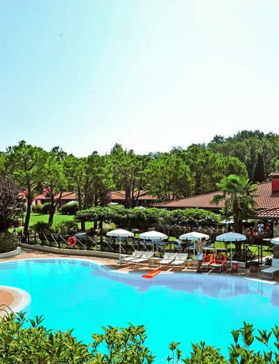 Poolanlage der Ferienanlage, eingebettet in eine weitläufige Gartenlandschaft mit Bäumen.