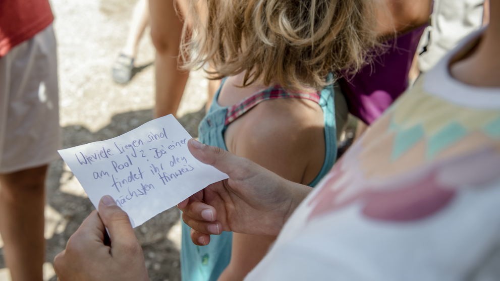 Kind gestaltet gemeinsam mit anderen Kindern ein kreatives Projekt im Rahmen eines Ferienprogramms.