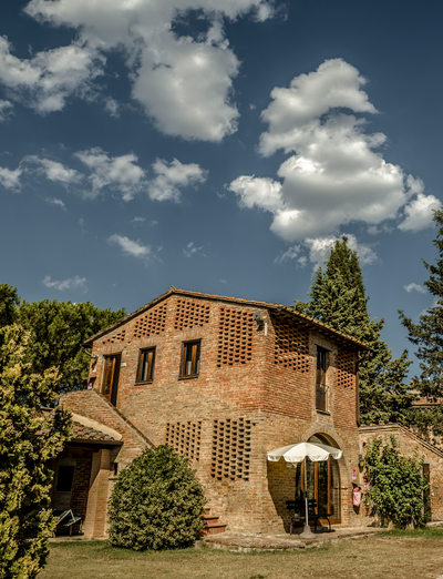 Historisches Natursteingebäude mit Garten und Zypressen unter blauem Himmel.