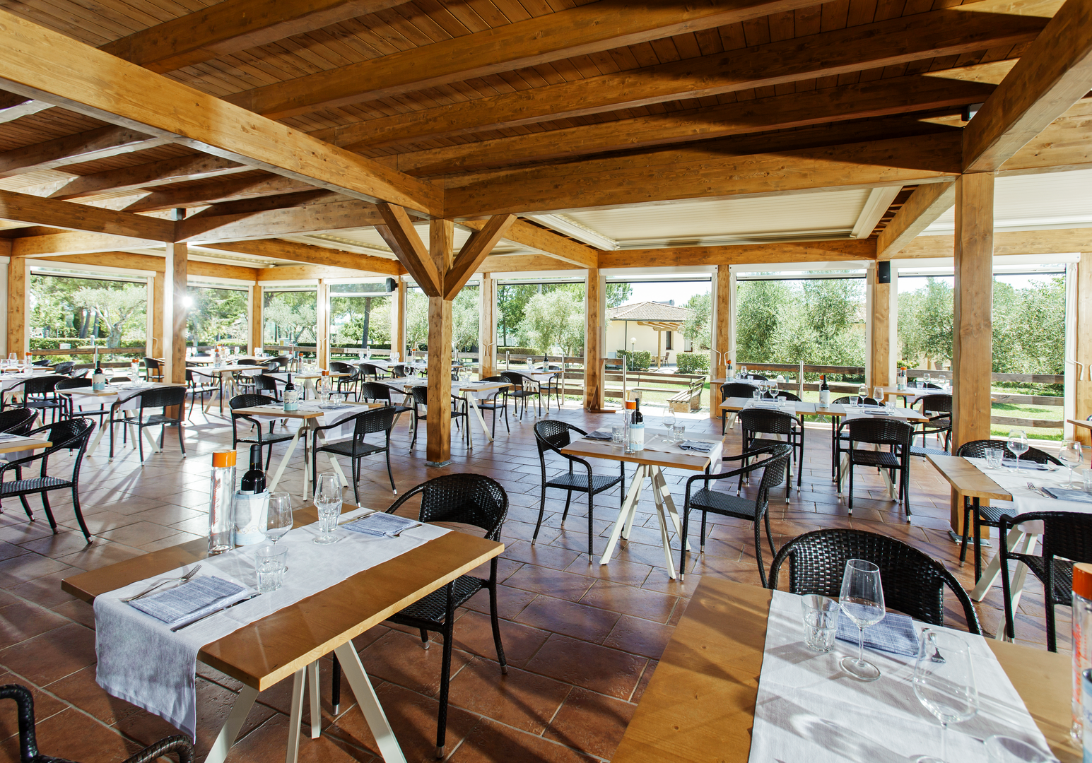 Großzügiger Restaurantbereich mit Holzdach und Blick auf die Gartenanlage der Ferienanlage.