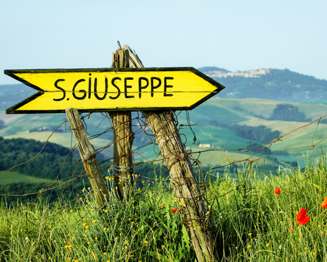 Holzwegweiser vor einer weiten Hügellandschaft mit Feldern und Weinbergen.